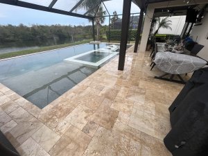 Cleaned travertine pool deck surrounding a screened infinity pool with lakefront view in Florida